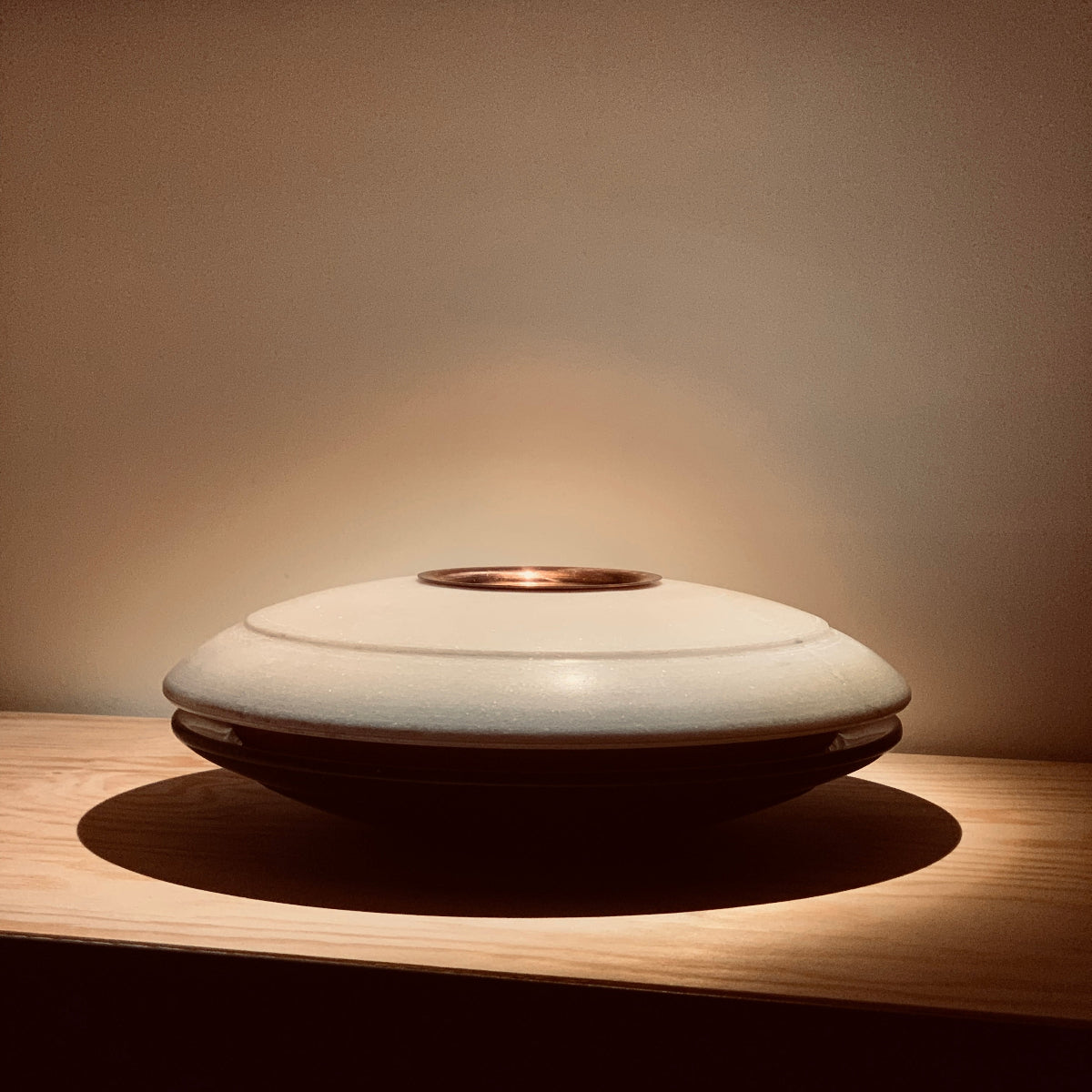 Two marble concave dishes facing each other with a copper bowl insert and a copper dish on top on a wooden surface with warm lighting