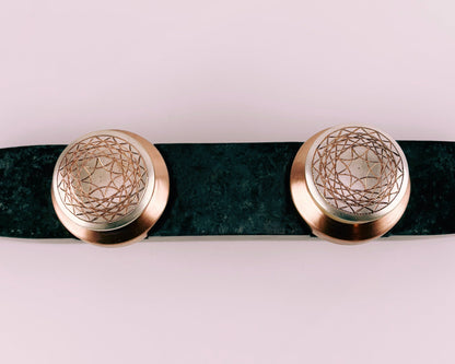 Prakasham Vallam are two small round containers made of copper and gilted with silver with etchers patterns  on a dark  green marble stone surface with a textured wall in the background.